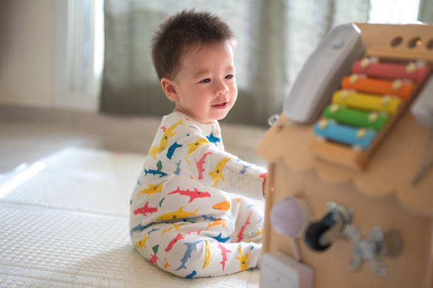 Baby boy playing with large activity box in the bedroom while sitting on a baby safe soft playmat on the floor at home. 10 months old infant playing at home