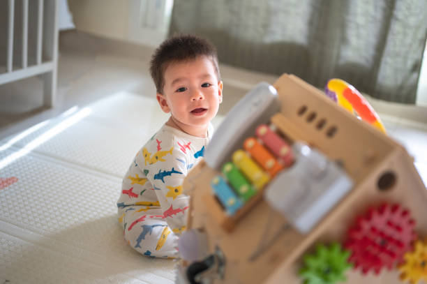 istock Baby boy playing with large activity box in the bedroom while sitting on a baby safe soft playmat on the floor at home. 10 months old infant playing at home 1402921907