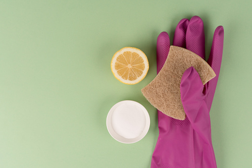 Natural household cleaners - natural sponge with baking soda or citric acid and lemon over green background with copy space. Homemade improvised cleaning products, green household concept