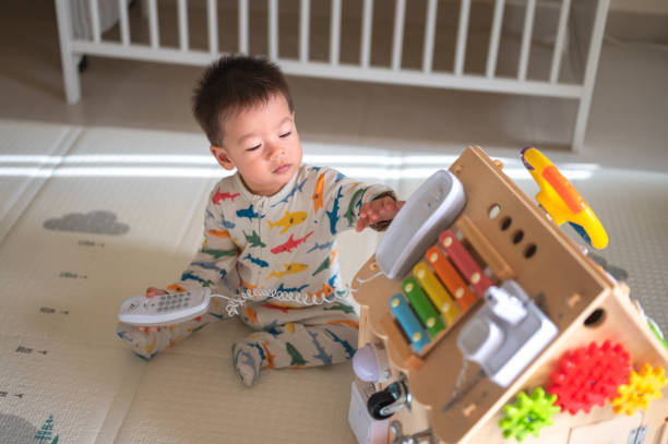 istock Baby boy playing with large activity box in the bedroom while sitting on a baby safe soft playmat on the floor at home. 10 months old infant playing at home 1402921933