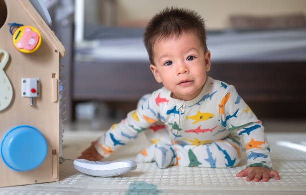 istock Baby boy playing with large activity box in the bedroom while sitting on a baby safe soft playmat on the floor at home. 10 months old infant playing at home 1402921995