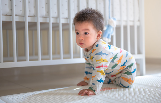 Mixed race baby boy crawling in the bedroom on a baby safe soft playmat on the floor at home. 10 months old infant starting to crawl to prepare for walking