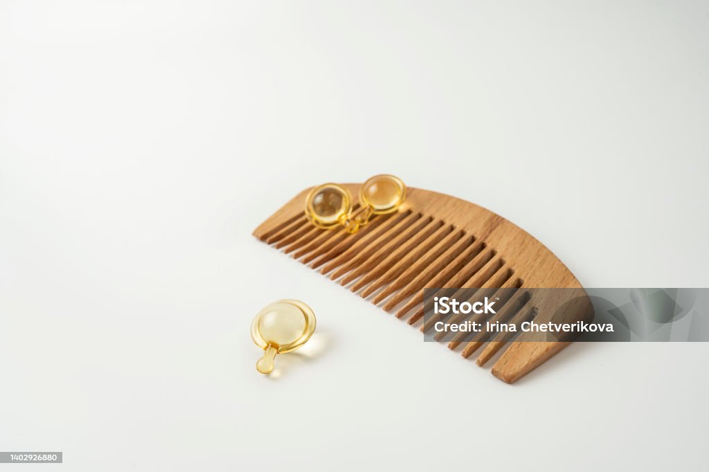 Natural oil vitamins golden capsules for hair lying on a wooden comb Booster Dose Stock Photo