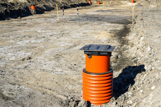New storm water drainage well with black iron grate cover and brown plastic sewer pipe on a new street construction site
