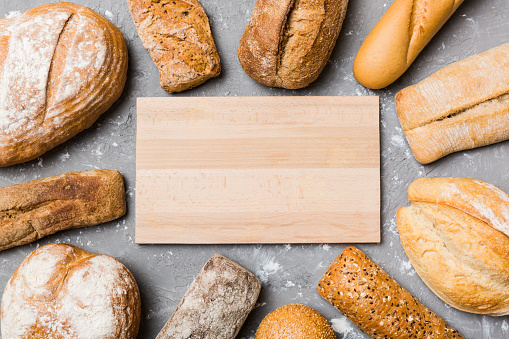Minimalist wooden cutting board blank mockup on background of Types of homemade bread. Different kinds of fresh bread as background, top view with space for your text or design.
