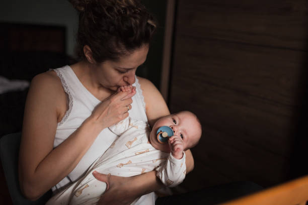 woman holding a baby and kissing its hand - mother baby new kissing imagens e fotografias de stock