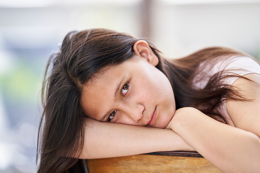 Portrait of dark-haired pre-adolescent girl looking at camera with her head in her arms