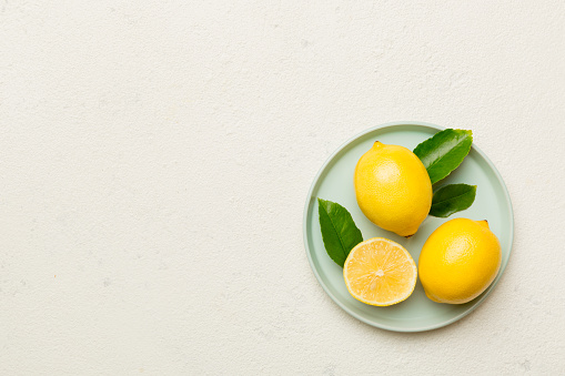 Fresh cutted lemon and whole lemons over round plate on colored background. Food and drink ingredients preparing. healthy eating theme top view vith copy space.