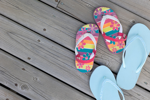 Two pairs of flip flop sandals, one light blue and the other with brightly coloured flowers on wood deck shot from above with copy space