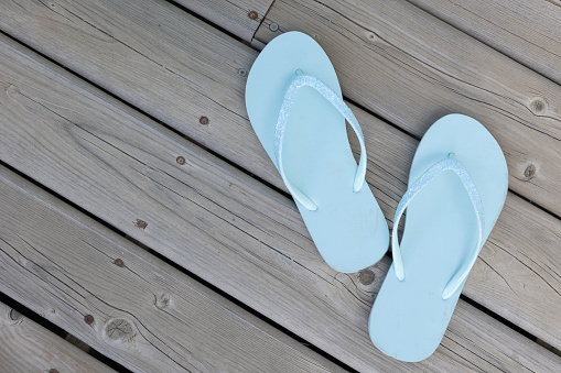 One pair of light blue flip flop sandals on a wood deck shot from above with copy space