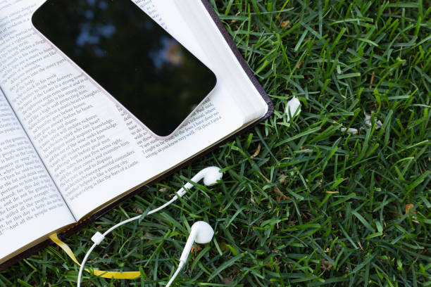Open bible with earbuds and device laying in the grass stock photo