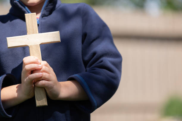 Young boy holding cross in his hands, face unseen Young boy holding wood Christian cross in his hands in front of himself, face unseen, with copy space beside him religion sunbeam one person children only stock pictures, royalty-free photos & images