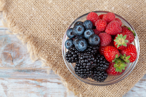 Fresh berries in a bowl on rustic wooden background.