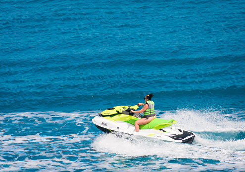 Royal Naval Dockyard, Bermuda- May 24, 2022- A tattooed  and sun burned female vacationer races her rented green and yellow Seadoo across the blue waters off the shore of the Royal Naval Dockyard in Bermuda.