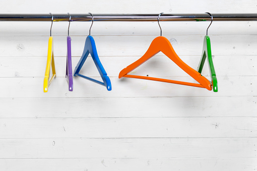 Group of multicolored hangers for garments on the black rack next to the white wall