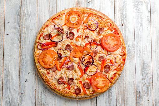 Italian meat pizza with hunter sausages, chicken and tomatoes with red onion and cheese top view on white wooden table