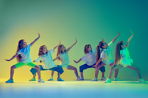 Grupo de niños, niñas con ropa deportiva de estilo casual bailando en clase de coreografía aisladas sobre fondo verde en luz de neón amarilla. Concepto de música, moda, arte photo