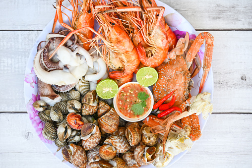 seafood plate with shrimp shellfish crab squid cockle spotted babylon with seafood sauce chili lemon lime serve on dining table, shrimps prawns seafood buffet menu cooked food