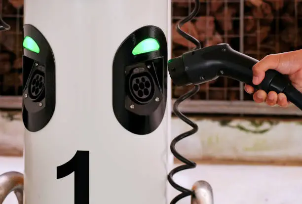 Close up of hand holding charging device, plugging into charging point station of car sharing electric vehicle in multi-storey carpark