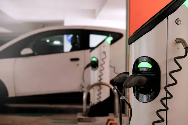 Charging station of white car sharing electric vehicle in indoor multi-storey carpark; selective focus