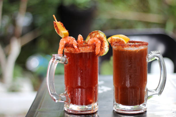 micheladas servidas en una mesa al aire libre, es una bebida alcohólica mexicana que se prepara mezclando cerveza, jugo de limón, chile, sal y camarones decorados con rodajas de naranja. - juice vegetable fruit vegetable juice fotografías e imágenes de stock