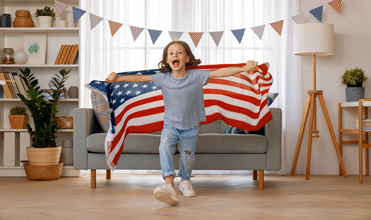 Patriotic holiday. Happy child girl with American flag at home. The USA celebrate 4th of July.
