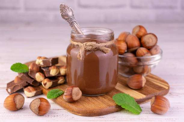 Chocolate spread with hazelnuts in a jar on a white wooden background.