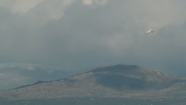Aircraft gaining height and flying over mountains in cloudy sky