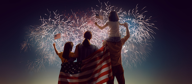 Patriotic holiday. Happy family, parents and daughters children girls with American flag outdoors. USA celebrate 4th of July.