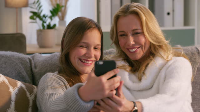 Carefree mother and daughter taking selfies together. Cheerful woman having fun with her child, taking a photo on a cellphone. Mother and child bonding, snuggling on the couch during a video call