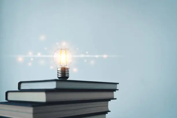 Glowing lightbulb or bright lamp with book or textbook. Skill improvement for student or businessperson. Studying and training course online at home. Business success idea, education learning concept