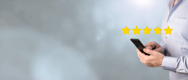 Businessman Evaluating Mobile App On Cellphone With 5 Five Stars on gray Background. Satisfaction survey concept. Customer hand touching to phone 5 stars. wide banner Customer hand touching to phone 5 stars virtual screening monitor for satisfaction evaluation survey and review. Satisfaction survey concept. wide banner goldco reviews personal stock pictures, royalty-free photos & images