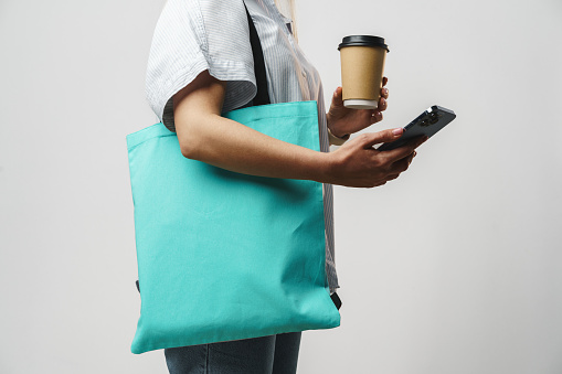 Cropped woman with cotton bag and paper coffee cup, studio shot, close up