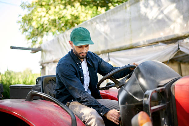 Three-quarter front view of bearded man in work clothes and cap sitting in driver’s seat and turning ignition on or off.