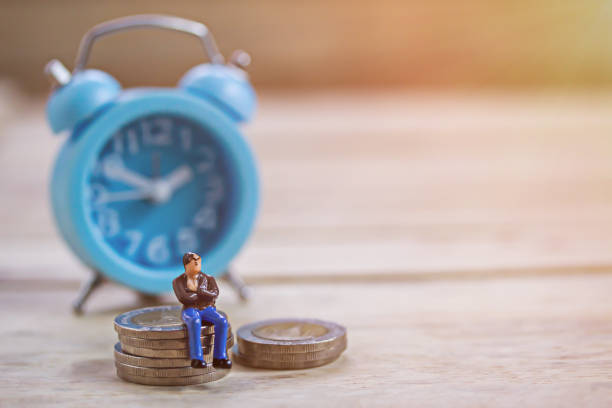 istock Miniature people sitting on coin and alramclock 1403005617
