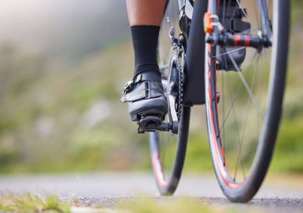 close-up de uma mulher pedalando lá fora. atleta esportiva em forma com os pés em pedais de bicicleta enquanto andava de bicicleta em uma estrada para exercícios. resistência e cardio durante um treino e treinamento - pedal bicycle sports training cycling - fotografias e filmes do acervo