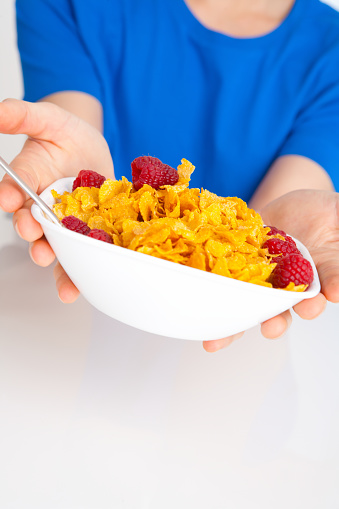 Man hand  in blue shirt showing bowl of corn flakes on white kitchen table.