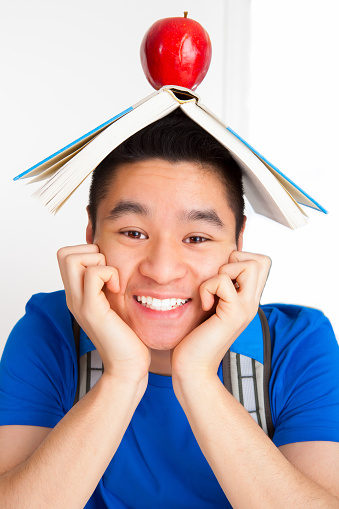 Smiling Vietnamese adult student in blue shirt with textbook and an apple on head.