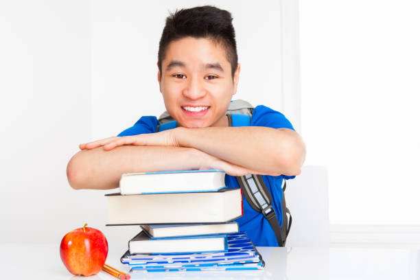 Smiling Vietnamese young adult student in blue shirt with a stack of textbooks.
