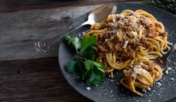 Traditional italian Spaghetti Bolognese. Served on a black plate with parmesan cheese on rustic and wooden table background. Closeup and side view with copy space