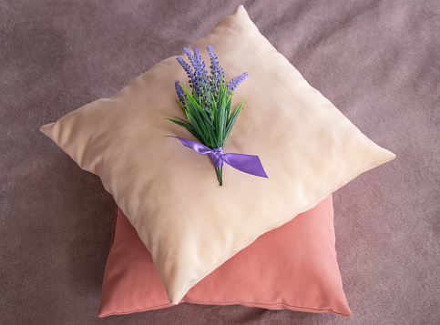 Top view of  color pillows on velvet blanket covered sofa and bouquet of lavender on top of them. Preparation hotel room for guests by decorating bed with fresh flowers.