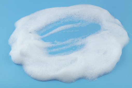 White soap or shampoo foam bubbles on blue background.