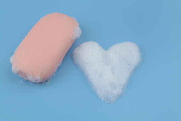 istock Soap bar and heart shaped foam bubbles on blue background. 1403017368