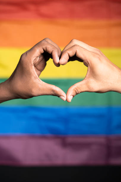 vertikale nahaufnahme von händen, die liebe oder herzsymbol vor der pride- oder regenbogenflagge machen - konzept der schwulen paarliebe, solidarität und der feier des pride-monats. - pride lgbtqi veranstaltung stock-fotos und bilder
