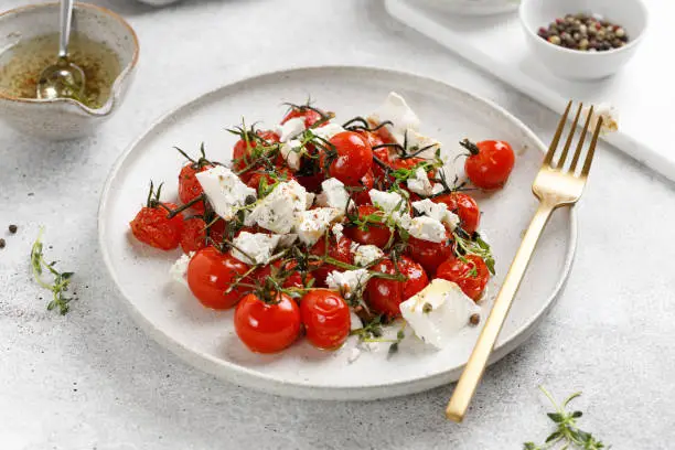 Photo of Baked cherry tomatoes and Feta cheese with oil, garlic and thyme in white plate. Diet dinner salad idea.