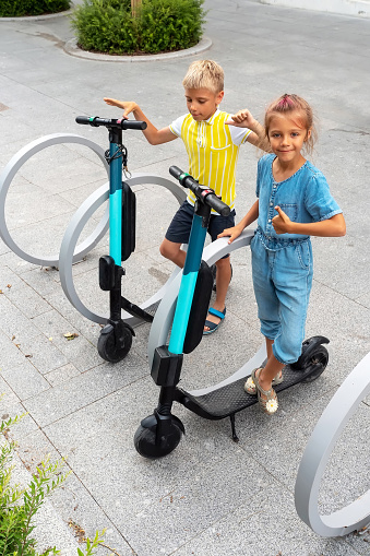 Happy kids standing on electric scooter at parking lot outdoor. Eco friendly green modern urban mobility concept of sharing transportation with electric scooters for rent