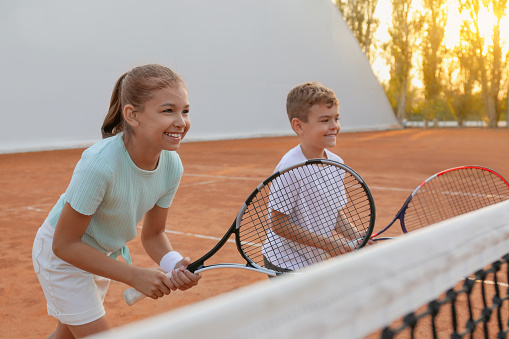 Happy children playing tennis on court outdoors