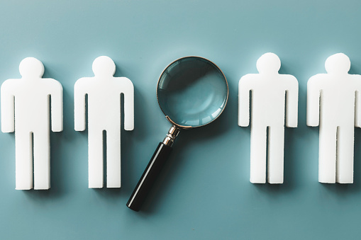 Recruitment, human resource and survey concept . Represented by a row of man and woman models in a row and one magnifying glass on blue background.