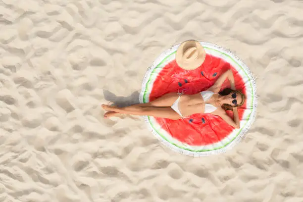 Photo of Woman sunbathing on round beach towel at sandy coast, aerial view