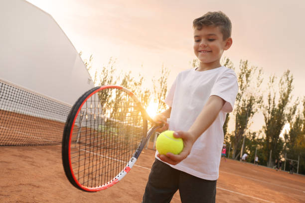 mignon petit garçon jouant au tennis sur le court à l’extérieur - little boys only outdoors little boys elementary age photos et images de collection